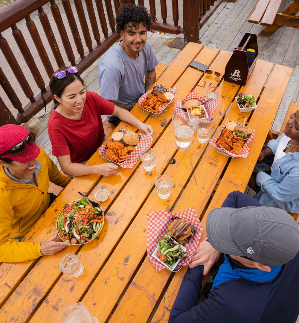 A group of friends enjoys food and drinks on a patio at Sunshine ski resort in Banff National Park. 